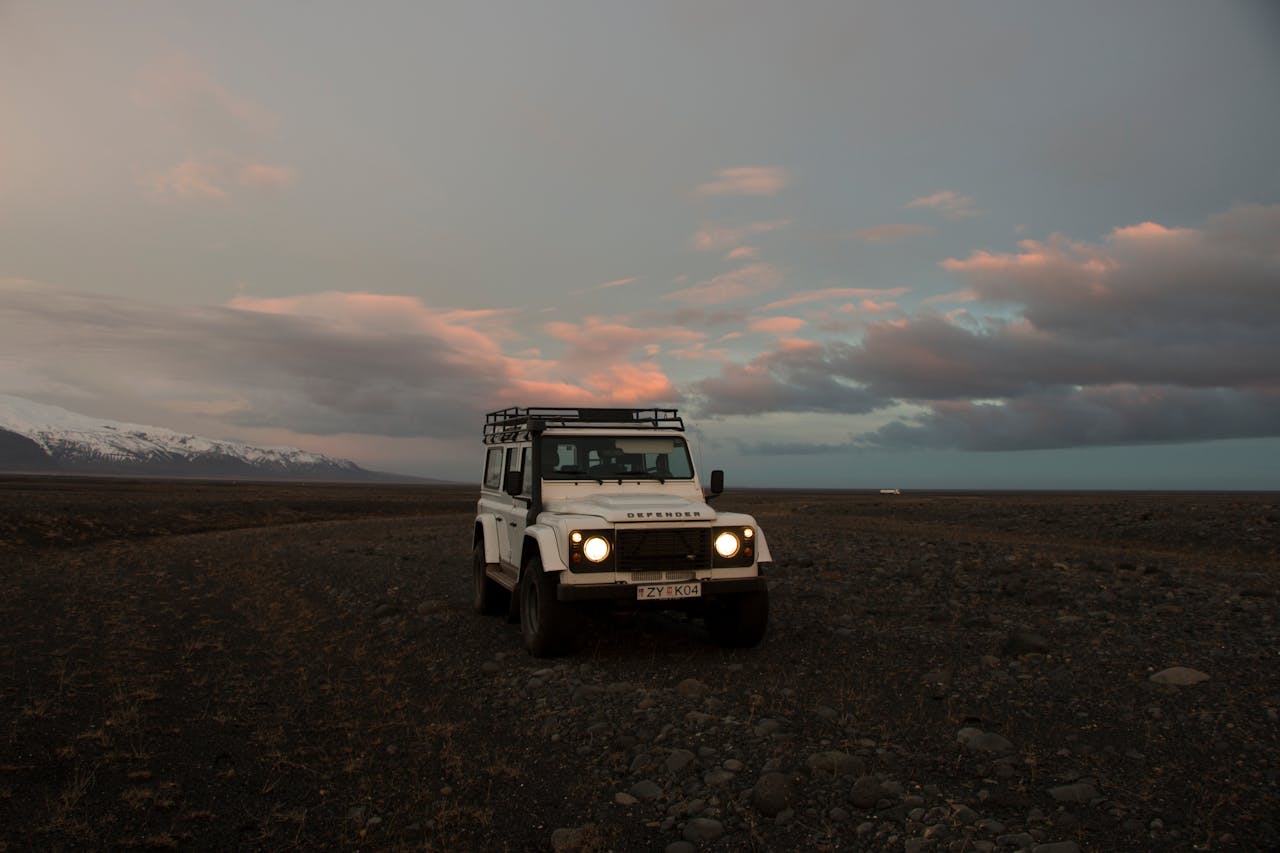A Land Rover Defender parked on rocky terrain with stunning mountain backdrop at dusk.