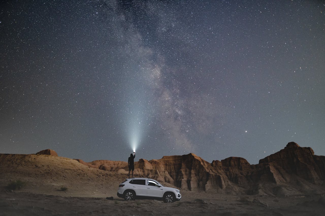 journey A person with a flashlight stands near an SUV under a star-filled desert sky, perfect for adventure seekers and stargazers.