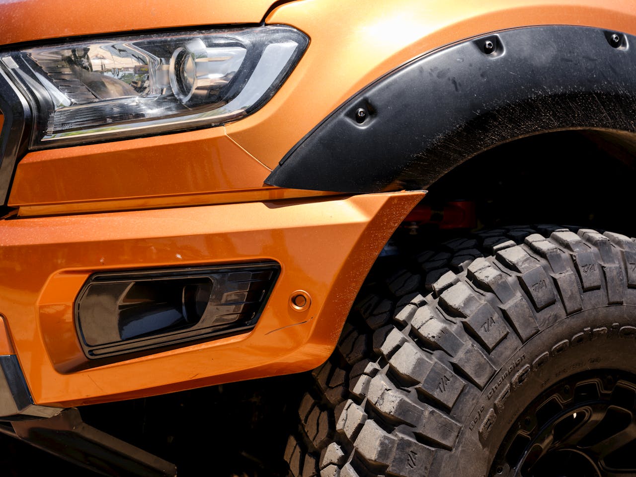 services-02 Detailed shot showcasing the rugged tire and headlight of an orange off-road vehicle, highlighting design and durability.