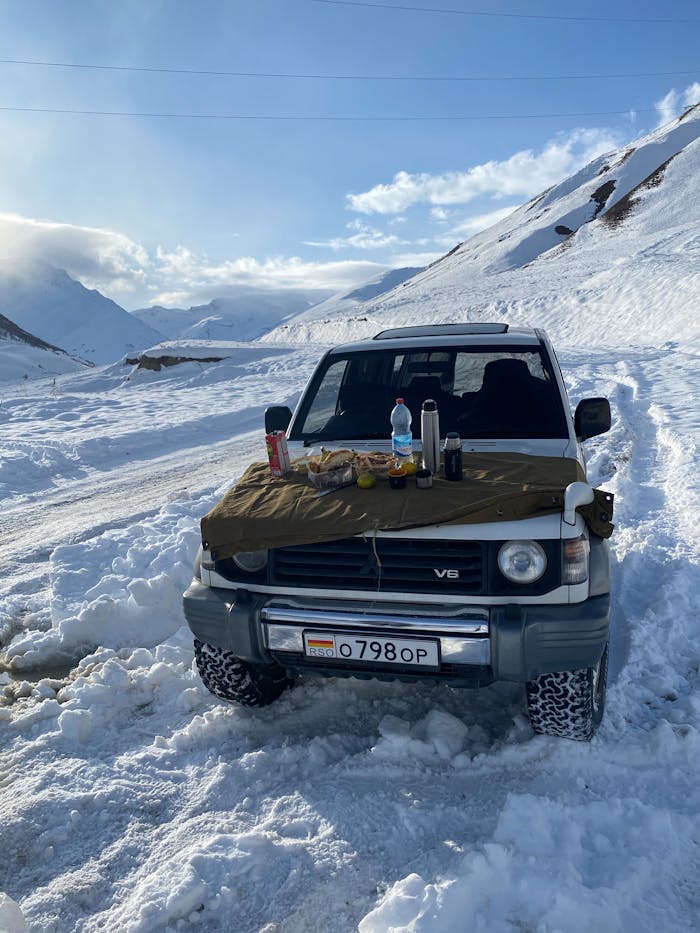 services-01 SUV on snowy mountain road with picnic setup on hood. Adventure travel scene.